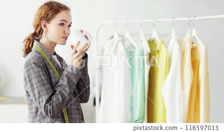 Successful Red-Haired Tailor Drinking Coffee Standing In Her Showroom. Copy Space, Selective Focus Successful Red-Haired Tailor Drinking Coffee Standing In Her Showroom. Copy Space, Selective Focus 116597013
