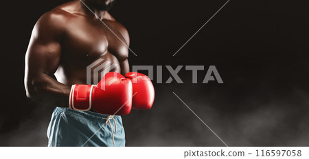 A shirtless boxer wearing red boxing gloves stands in a fighting stance against a black background with smoke. 116597058