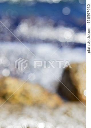 Sea waves rolling and crashing on the rocks with lots of white bokeh spots of sun glare on the surface of the ripples on the water. Sea view on a sunny summer day. Blurred abstract natural background 116597080