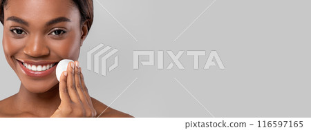 Smiling pretty millennial african american woman wiping her face with cotton pad, isolated on gray background, copy space. Routine procedures, makeup removal. Beauty spa day, skin care and cosmetics Smiling pretty millennial african american woman wiping her face with cotton pad, isolated on gray background, copy space. Routine procedures, makeup removal. Beauty spa day, skin care and cosmetics 116597165