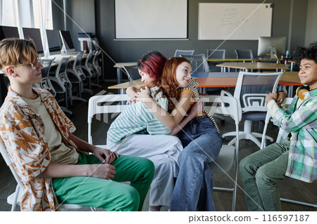 Two ethnically diverse gen alpha teen girls hugging each other at group therapy session at school, copy space 116597187