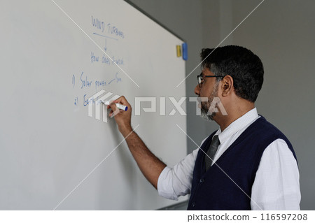 Medium closeup of mature biracial teacher writing on board during ecology class at school, copy space Medium closeup of mature biracial teacher writing on board during ecology class at school, copy space 116597208