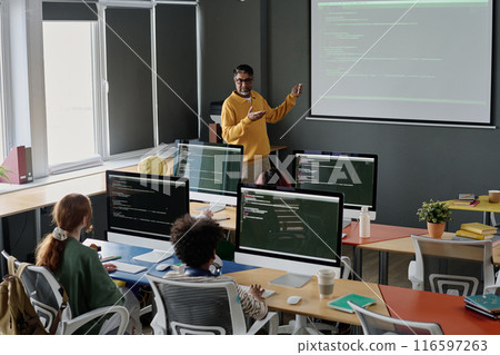 Mature biracial teacher of Computer Science explaining subject to group of teenagers during lesson at school Mature biracial teacher of Computer Science explaining subject to group of teenagers during lesson at school 116597263