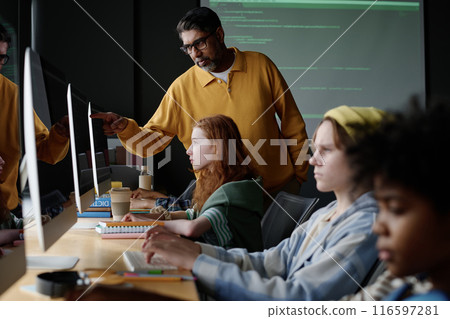 Mature biracial Computer Science teacher helping Caucasian girl to find mistake in code during lesson in modern classroom Mature biracial Computer Science teacher helping Caucasian girl to find mistake in code during lesson in modern classroom 116597281