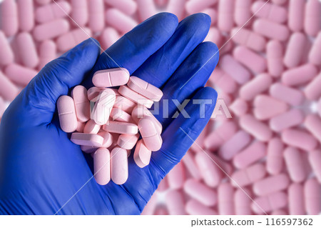 Doctor hand in blue gloves holding handful of pills above with pink pills background. Top view 116597362