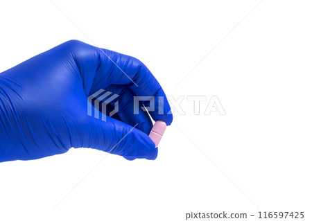 Hand in a blue glove holding a pink pill isolated on white background. Closeup 116597425
