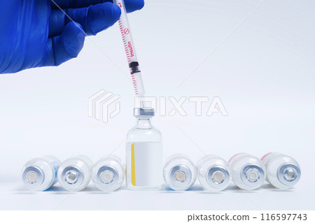Doctor hand with blue gloves holding syringe on top of vaccine bottle on white background 116597743