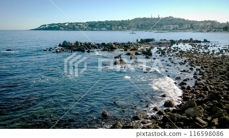 Foamy waves of a sea blue water rocks of the shore in Antibes, France Foamy waves of a sea blue water rocks of the shore in Antibes, France 116598086