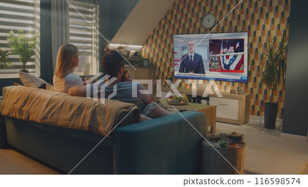 Caucasian couple watches news broadcast about United States Election Day on TV Caucasian couple watches news broadcast about United States Election Day on TV 116598574