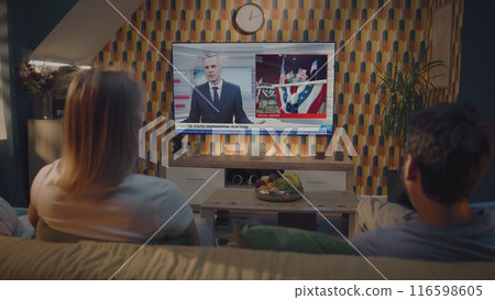 Couple watches news broadcast about US presidential elections on TV at home 116598605