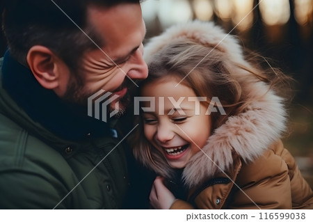 A father and daughter laugh together in a wooded area 116599038
