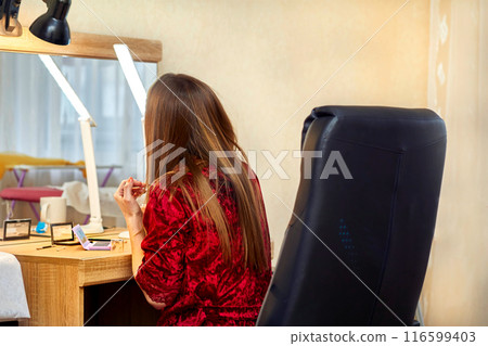 Young woman in a red housecoat applies makeup.Home mirrored dressing table Young woman in a red housecoat applies makeup.Home mirrored dressing table 116599403