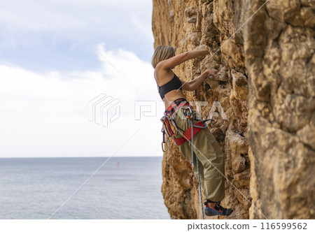 A woman is climbing a rock wall while wearing a black tank top and red 116599562