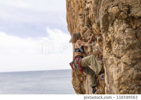 A woman is climbing a rock wall with a red and yellow harness 116599563