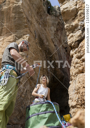 A man and a woman are standing in a cave with a green bag 116599617