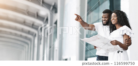 A couple, a Black man and a Black woman, are smiling and looking at a map in an airport terminal. The man is pointing at something, copy space A couple, a Black man and a Black woman, are smiling and looking at a map in an airport terminal. The man is pointing at something, copy space 116599750