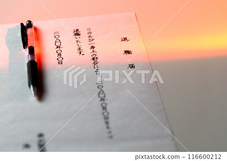 在略帶紅色的燈光下，在白色桌子上用黑色中性墨水筆手寫的辭職信拍攝的場景。 116600212