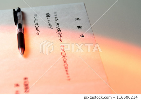 A scene with a handwritten resignation letter and a black gel ink pen on a white table, shot with a slightly orange-tinted light 116600214