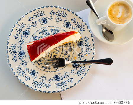 Piece of a tasty strawberry cheesecake served on a painted ceramic plate plate near a cup of coffee in the cafe Piece of a tasty strawberry cheesecake served on a painted ceramic plate plate near a cup of coffee in the cafe 116600776