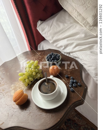 Breakfast in bed. Cup of coffee with fresh fruits on a wooden table in a hotel room. Breakfast in bed. Cup of coffee with fresh fruits on a wooden table in a hotel room. 116601292