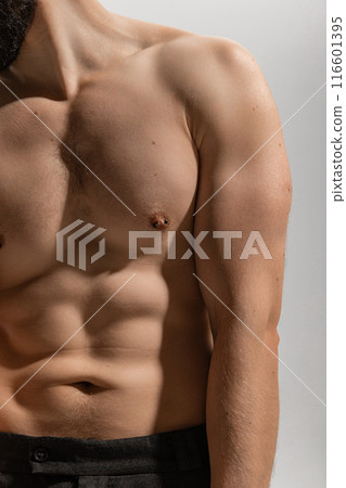 Cropped photo of shirtless young man wearing black pants, showing his upper body, torso against grey studio background. 116601395