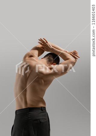 Rear view of shirtless man in black pants, emphasizing his toned back and athletic physique against grey studio background. 116601403