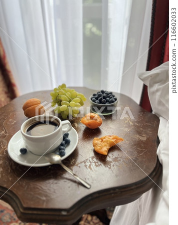 Cup of coffee with fresh fruits on the bedside table in a hotel room with red curtains Cup of coffee with fresh fruits on the bedside table in a hotel room with red curtains 116602033