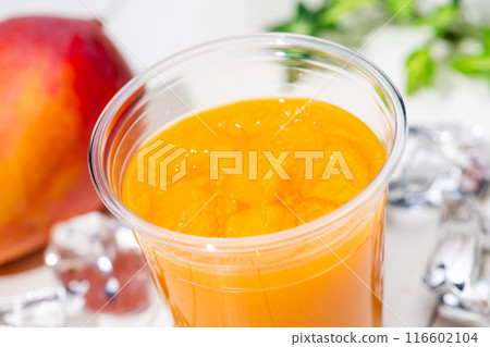 Close-up of mango smoothie in a plastic cup on a white table 116602104