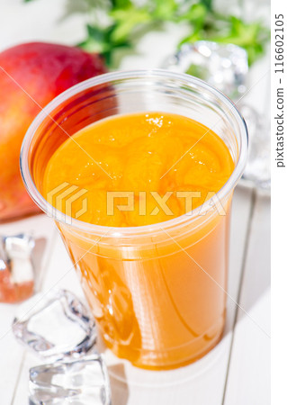 Close-up of mango smoothie in a plastic cup on a white table 116602105