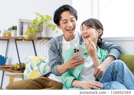 Young couple looking at a smartphone in the living room Young couple looking at a smartphone in the living room 116602569