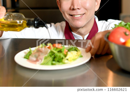 Male chef pouring olive oil onto salad Male chef pouring olive oil onto salad 116602621