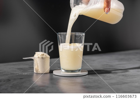 Protein drink. Pouring whey, vanilla protein shake drink in a glass. Food supplements. Dark background. Bodybuilding, fitness, gym. 116603673