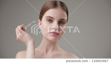 Beauty, health, cosmetics, anti-aging therapy and skin care concept - young beautiful brunette Caucasian woman applying cosmetic serum from a pipette for facial skin care 116603867