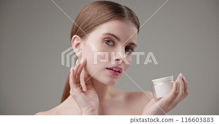 Beauty, health, cosmetics, anti-aging therapy and skin care concept - young beautiful brunette Caucasian woman holds a jar of moisturizer in her hands and applies the cream to her face skin 116603883