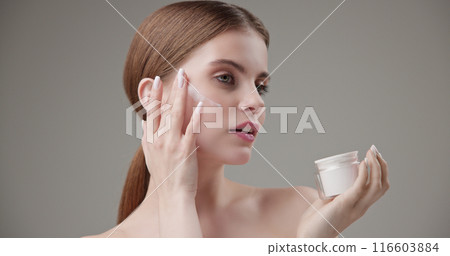 Beauty, health, cosmetics, anti-aging therapy and skin care concept - young beautiful brunette Caucasian woman holds a jar of moisturizer in her hands and applies the cream to her face skin Beauty, health, cosmetics, anti-aging therapy and skin care concept - young beautiful brunette Caucasian woman holds a jar of moisturizer in her hands and applies the cream to her face skin 116603884