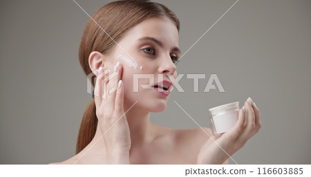 Beauty, health, cosmetics, anti-aging therapy and skin care concept - young beautiful brunette Caucasian woman holds a jar of moisturizer in her hands and applies the cream to her face skin 116603885
