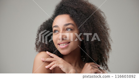 Beauty and healthcare concept - beautiful African American woman with curly afro hairstyle and clean, healthy skin touching face with hand, doing facial massage, posing and looking at camera Beauty and healthcare concept - beautiful African American woman with curly afro hairstyle and clean, healthy skin touching face with hand, doing facial massage, posing and looking at camera 116603892