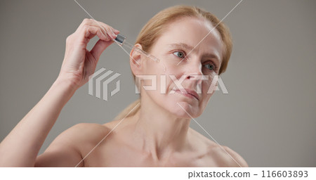 Real people - concept of age, beauty, health and dry skin care - beautiful mature Caucasian middle aged woman in her 50s applying skin care serum to her face 116603893