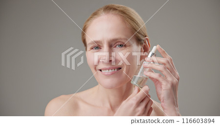 Real people - age, beauty, health and dry skin care concept - beautiful mature Caucasian middle aged woman in her 50s holding a bottle of skin care serum Real people - age, beauty, health and dry skin care concept - beautiful mature Caucasian middle aged woman in her 50s holding a bottle of skin care serum 116603894