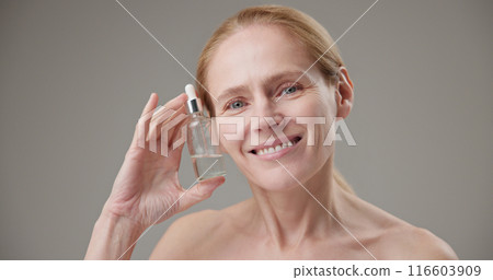 Real people - age, beauty, health and dry skin care concept - beautiful mature Caucasian middle aged woman in her 50s holding a bottle of skin care serum 116603909