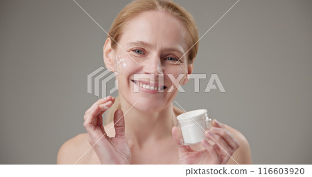 Real people - age, beauty, health and dry skin care concept - beautiful mature Caucasian middle aged woman in her 50s applying moisturizer to her face Real people - age, beauty, health and dry skin care concept - beautiful mature Caucasian middle aged woman in her 50s applying moisturizer to her face 116603920