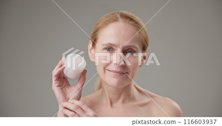 Real people - concept of age, beauty, health and dry skin care - beautiful mature Caucasian middle aged woman in her 50s holding a jar of moisturizer in her hands 116603937