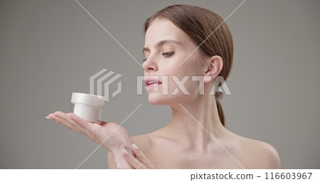 Beauty, health, cosmetics, anti-aging therapy and skin care concept - young beautiful brunette Caucasian woman holding a jar of moisturizer in her hands and looking at the camera 116603967
