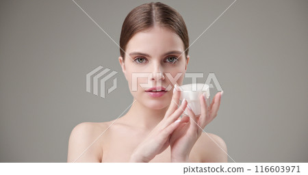 Beauty, health, cosmetics, anti-aging therapy and skin care concept - young beautiful brunette Caucasian woman holding a jar of moisturizer in her hands and looking at the camera 116603971