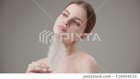 Beauty, health, cosmetics, anti-aging therapy and skin care concept - young beautiful brunette Caucasian woman holding a white fluffy feather in her hands, tenderness, lightness and softness Beauty, health, cosmetics, anti-aging therapy and skin care concept - young beautiful brunette Caucasian woman holding a white fluffy feather in her hands, tenderness, lightness and softness 116604010