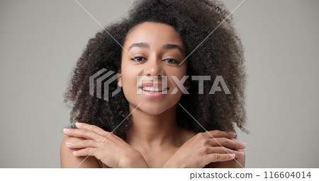 Beauty and healthcare concept - beautiful African American woman with curly afro hairstyle and clean, healthy skin touching face with hand, doing facial massage, posing and looking at camera Beauty and healthcare concept - beautiful African American woman with curly afro hairstyle and clean, healthy skin touching face with hand, doing facial massage, posing and looking at camera 116604014