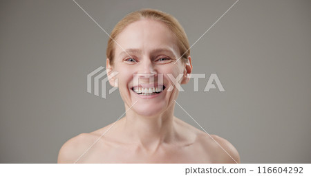 Real people - concept of age, beauty, health and dry skin care - beautiful mature Caucasian middle-aged woman in her 50s looks with a calm confident look at the camera, smiles a bright toothy smile 116604292