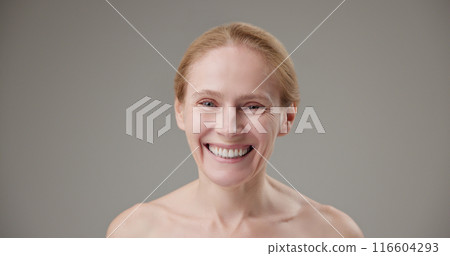 Real people - concept of age, beauty, health and dry skin care - beautiful mature Caucasian middle-aged woman in her 50s looks with a calm confident look at the camera, smiles a bright toothy smile 116604293