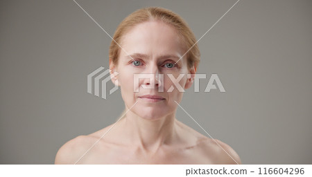 Real people - concept of age, beauty, health and dry skin care - beautiful mature Caucasian middle-aged woman in her 50s looks at the camera with a calm, confident look, closes and opens her eyes 116604296