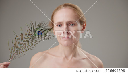 Real people - concept of age, beauty, health and dry skin care - beautiful mature middle-aged Caucasian woman in her 50s holding a peacock feather as a symbol of lightness and tenderness Real people - concept of age, beauty, health and dry skin care - beautiful mature middle-aged Caucasian woman in her 50s holding a peacock feather as a symbol of lightness and tenderness 116604298